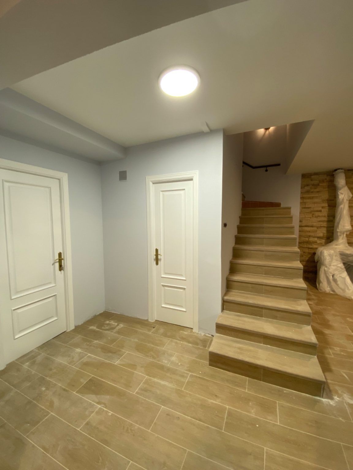 Pasillo con escaleras reformado, paredes pintadas y puertas lacadas en blanco