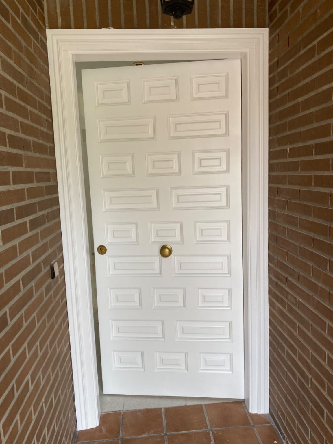 Puerta exterior lacada en blanco después de la reforma en vivienda con ladrillo visto